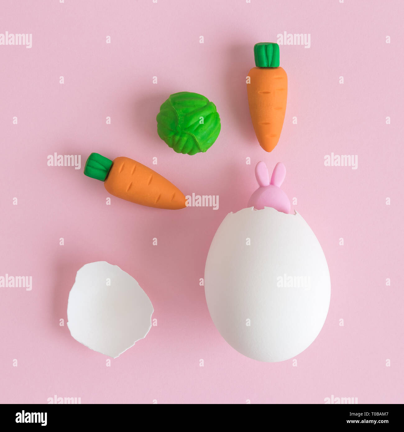 Piccolo bunny proveniente al di fuori del guscio delle uova e le carote con cavolo sul rosa pastello background creativo minima nozione di pasqua. Foto Stock