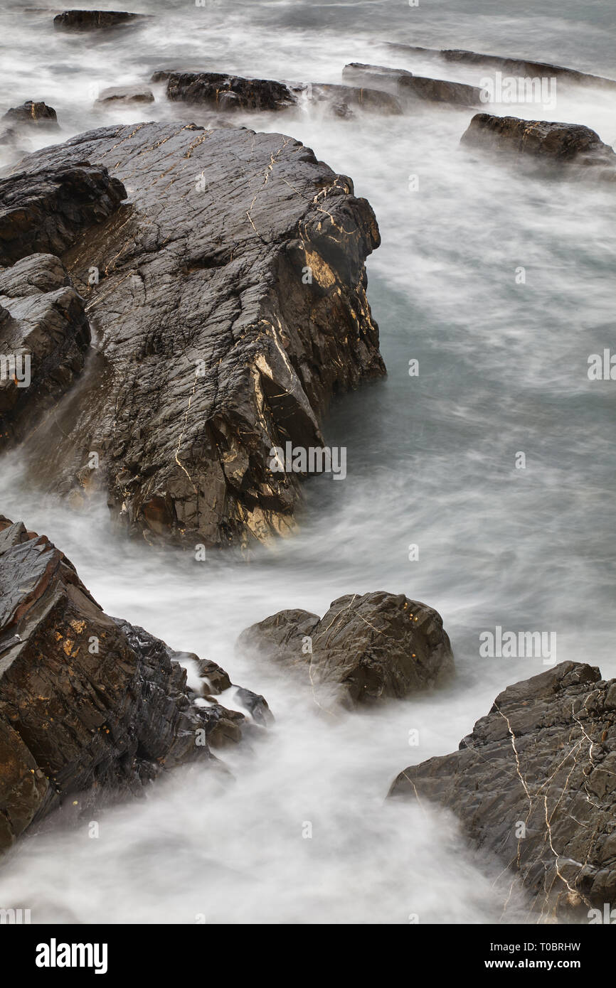 Atlantic surf intorno lavaggio rocce costiere al tramonto; a Hartland Quay, North Devon, Gran Bretagna. Foto Stock