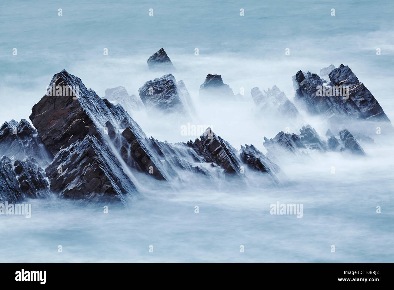 Atlantic surf intorno lavaggio rocce costiere al tramonto; a Hartland Quay, North Devon, Gran Bretagna. Foto Stock