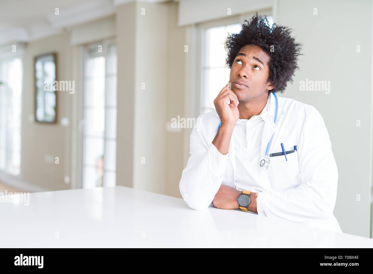 Americano africano uomo medico presso la clinica con la mano sul mento pensando di domanda, pensieroso espressione. Sorridente con premurosa faccia. Concetto di dubbio. Foto Stock