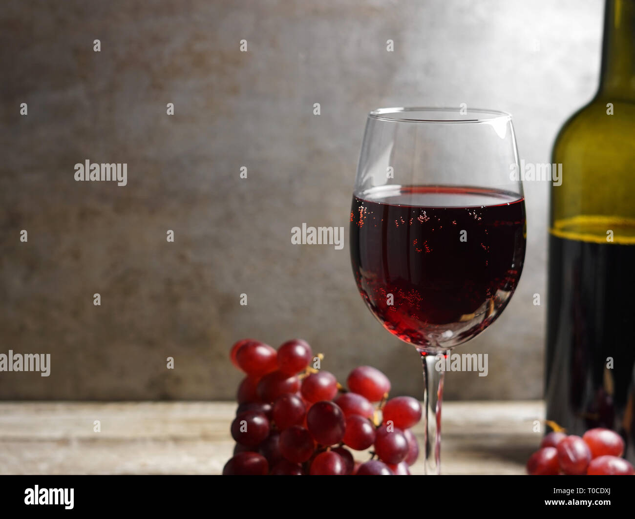 Bicchiere di vino rosso su una tavola di legno in un ambiente rustico e vintage wine bar con uve di frutta e una bottiglia di vino sul background closeup vista. Foto Stock