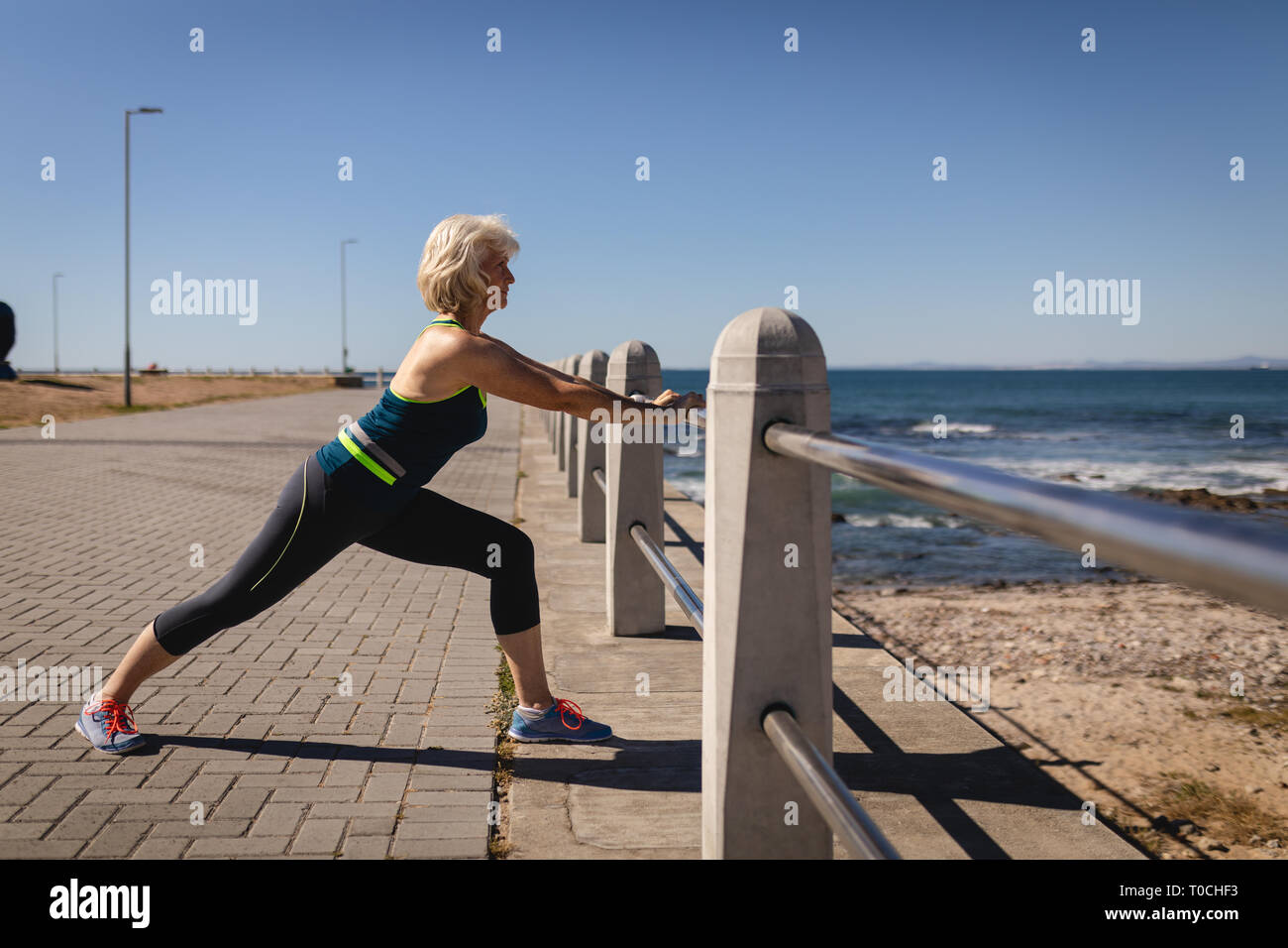 Attiva donna senior stretching sul lungomare vicino alla spiaggia Foto Stock