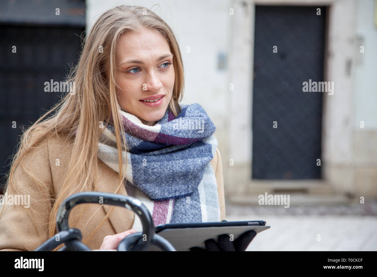 Bionda bella donna tenendo compressa sulla strada della citta'. Ritratto di giovane donna indossa foulard tartan in piedi fuori la creazione e l'utilizzo di tablet. Foto Stock