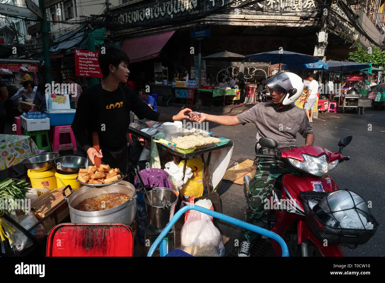 Un motociclista in Chinatown, Bangkok, si ferma ad acquistare fritte involtini primavera da un prodotto alimentare in stallo Foto Stock