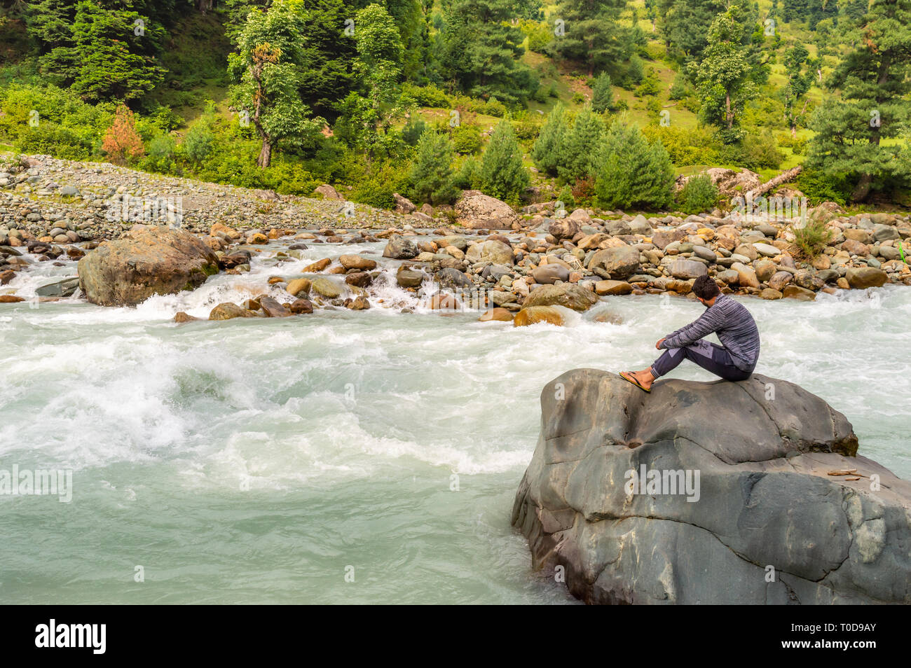 Una persona seduta su una roccia di fronte un fiume nella valle Lidder, a Pahalgam nel Kashmir Foto Stock