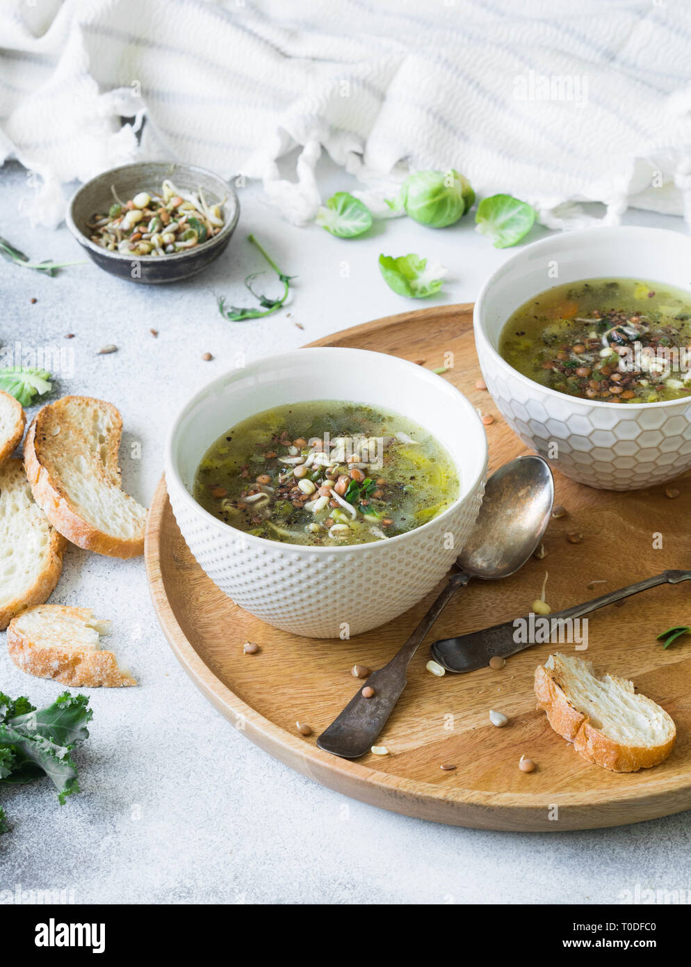 Vegetali verdi zuppa vegana da keil, i cavoli di Bruxelles, zucchine, porro con vari semi germinati e i germogli con crostini sul vassoio di legno sulla luce b Foto Stock