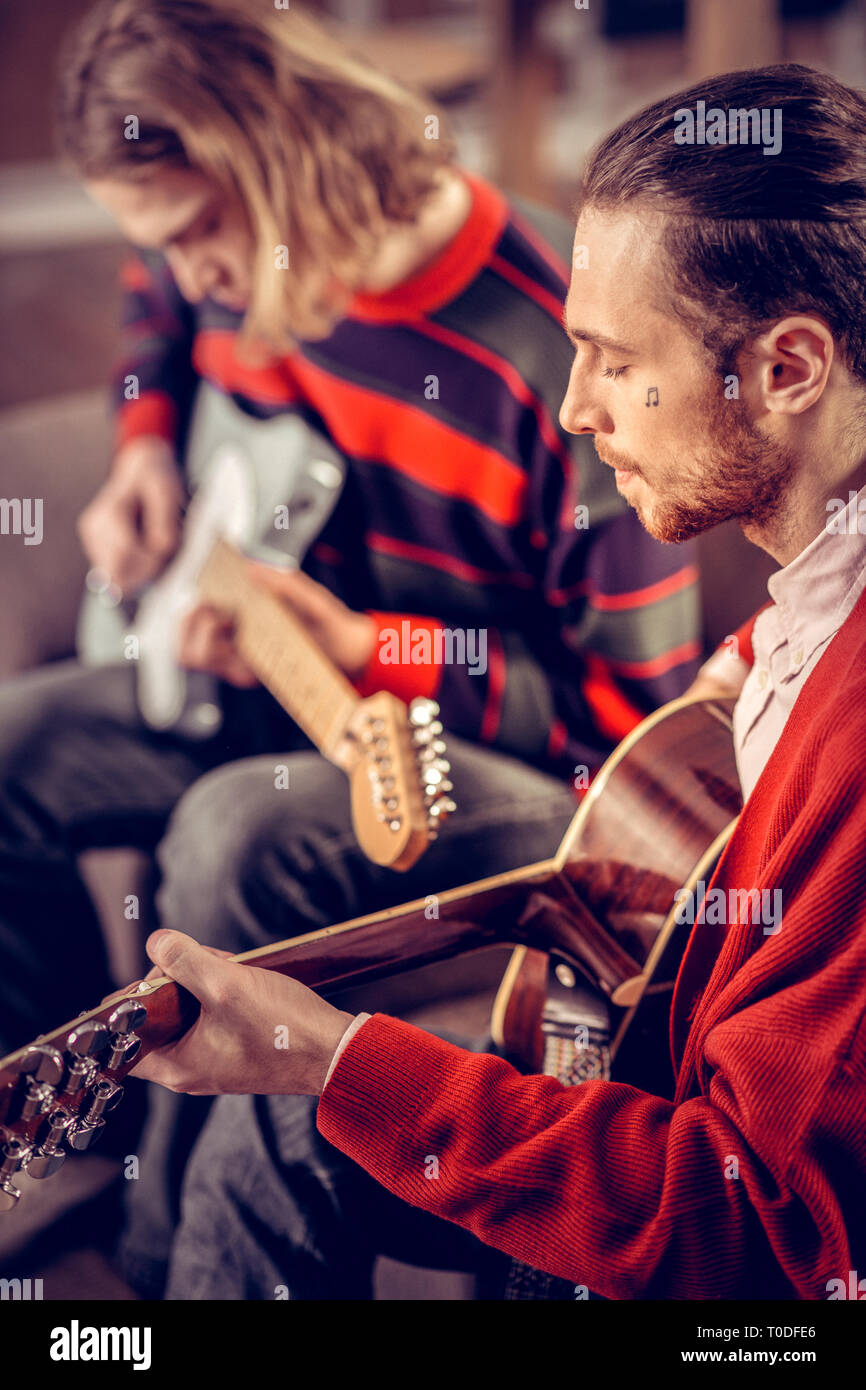 Musicista con poco tatuaggio sul suo volto a suonare la chitarra Foto Stock