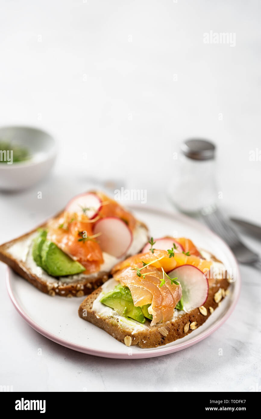 Toast con avocado, cetriolo e salmone su sfondo chiaro. Colazione sana nozione Foto Stock