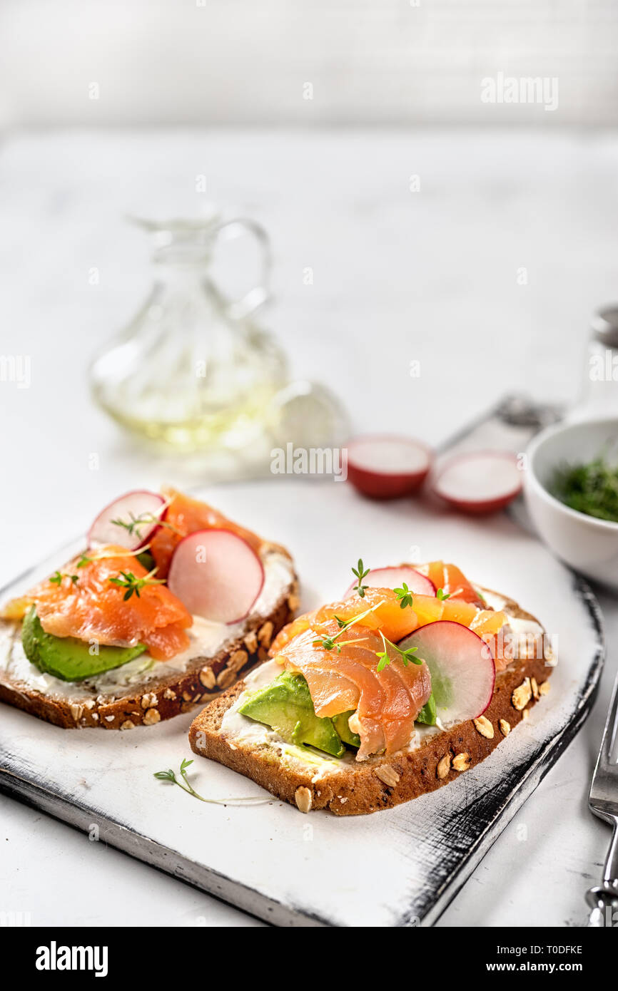 Toast con avocado, cetriolo e salmone su sfondo chiaro. Colazione sana nozione Foto Stock