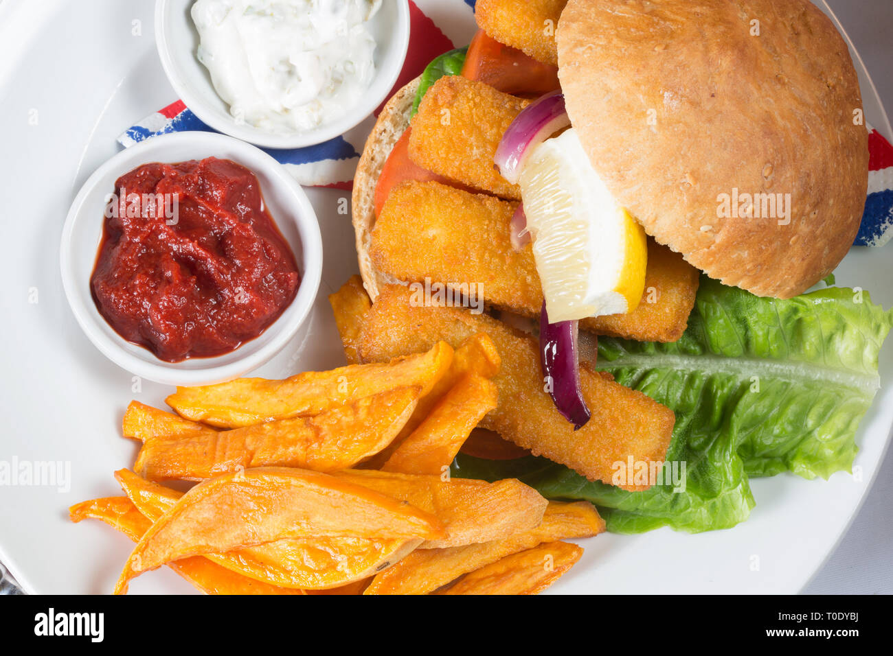 Inglese tipici snack per il pranzo di pesce le dita in un panino, patata dolce patate fritte servite con ketchup e il tartaro. Foto Stock