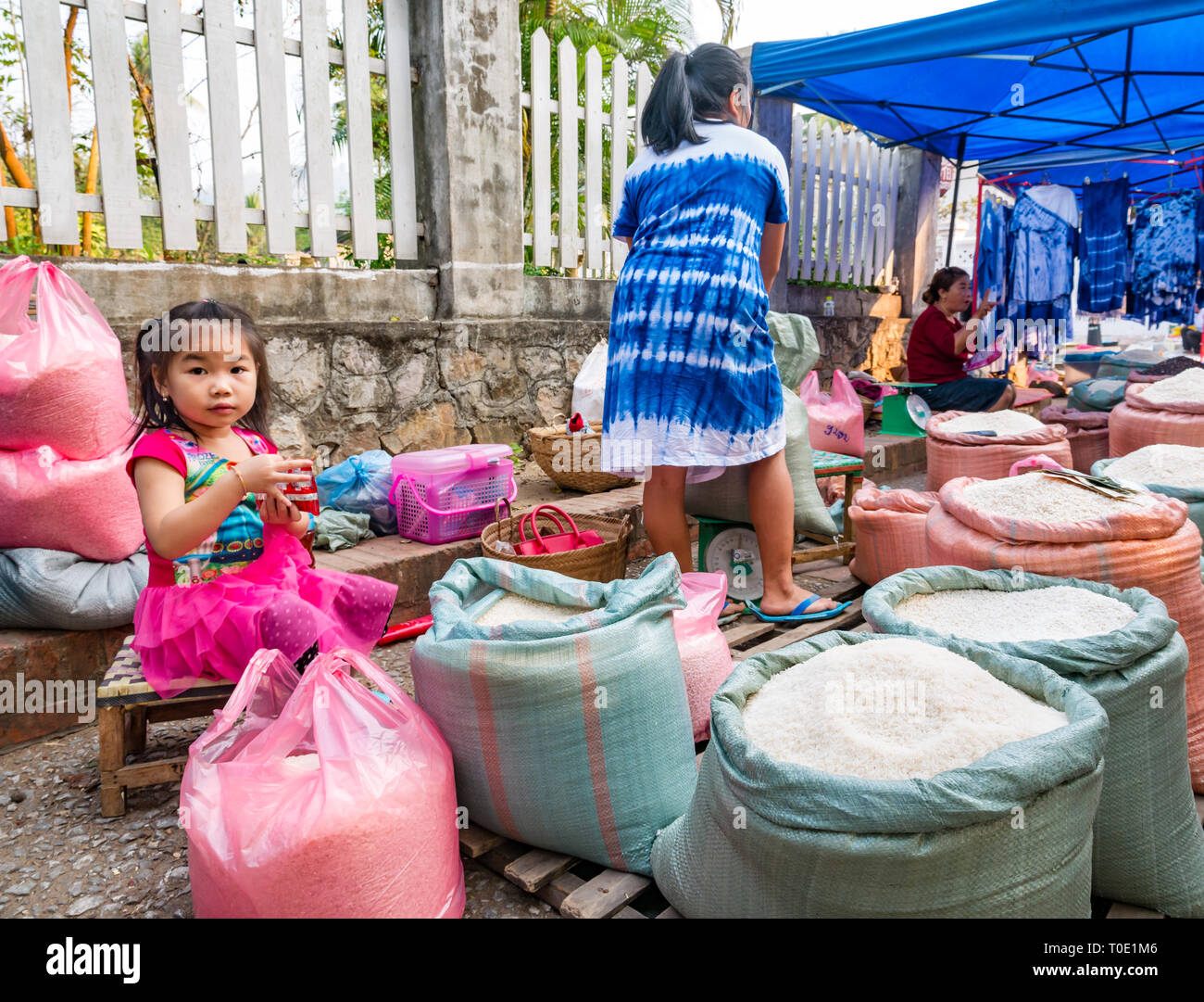 Bambina giocando accanto a madre al mercato del riso in stallo, mattina street market alimentare, Luang Prabang, Laos, SE Asia Foto Stock