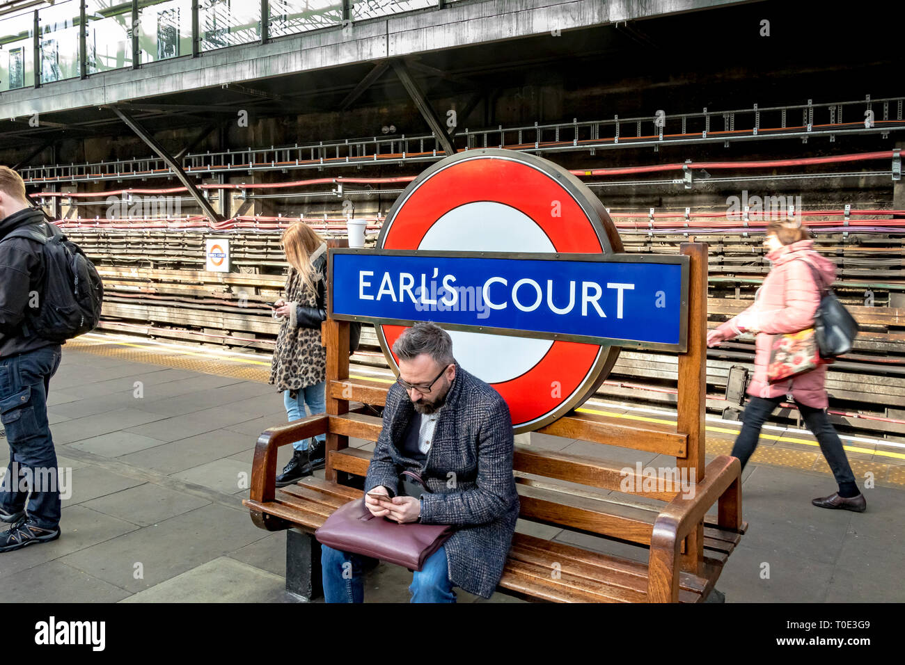 Un uomo seduto su una panchina alla stazione della metropolitana di Earls Court, Londra, Regno Unito Foto Stock