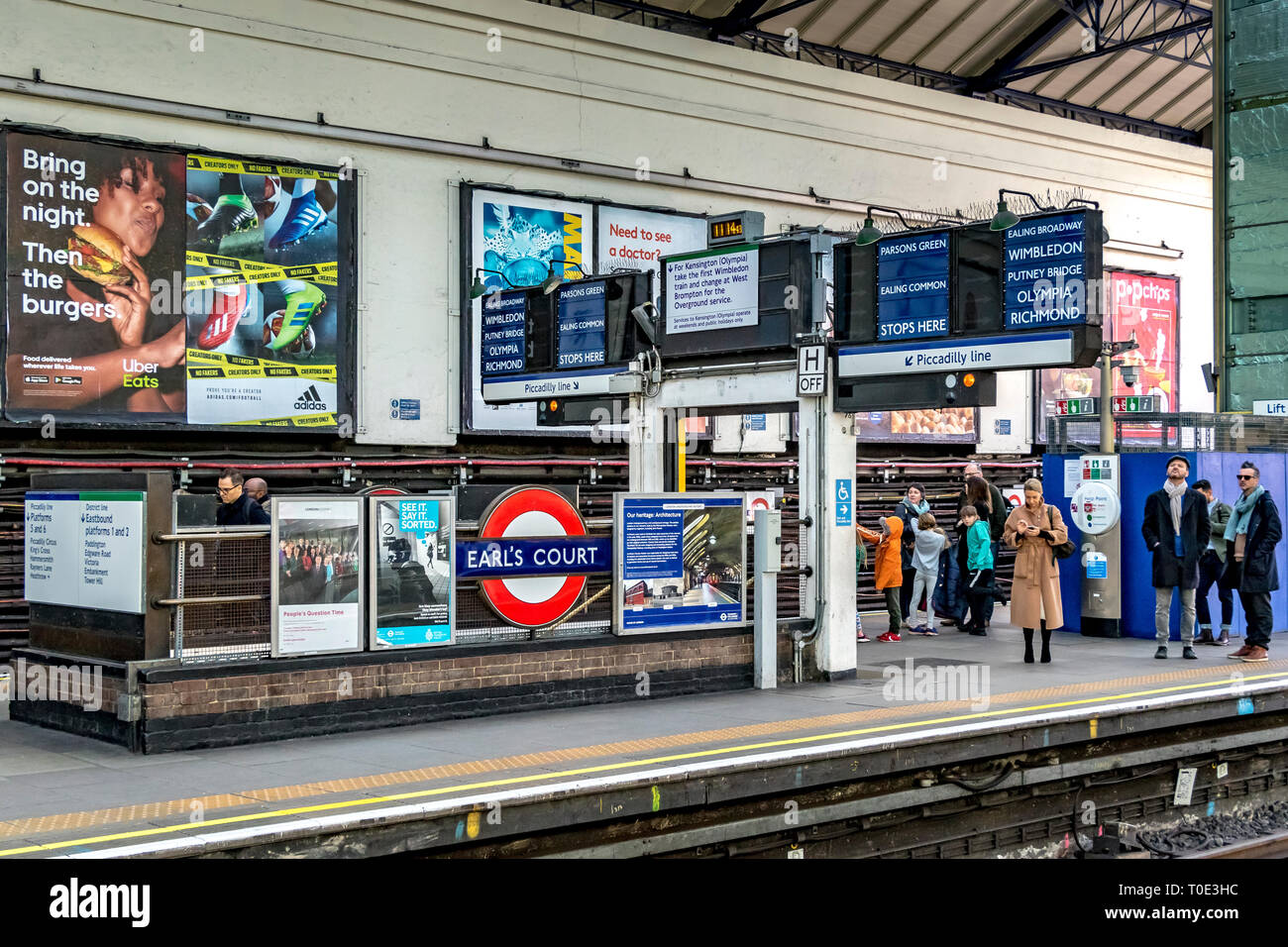 Persone che aspettano sulla piattaforma per un treno District Line alla stazione della metropolitana di Earls Court , Londra, Regno Unito Foto Stock