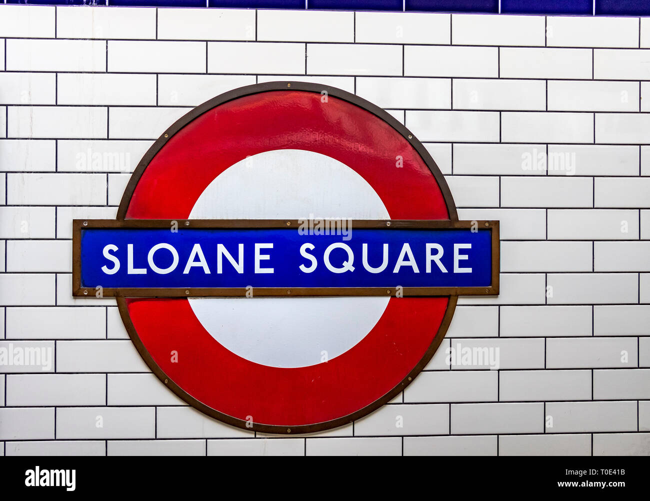 Segno della stazione della metropolitana di Sloane Square o rotonda contro pareti piastrellate di ceramica bianca, stazione della metropolitana di Sloane Square, Londra UK Foto Stock