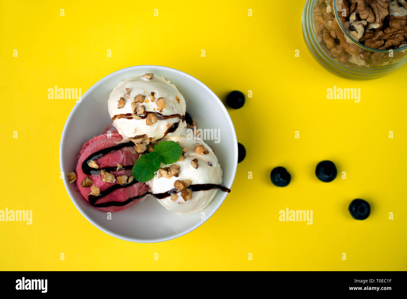 Vanila e gelato alla fragola con caramello e menta su bianco ciotola con dadi e mirtilli su sfondo giallo. Tre convogliatori, splendidi dessert. Scatto dall'alto. Foto Stock