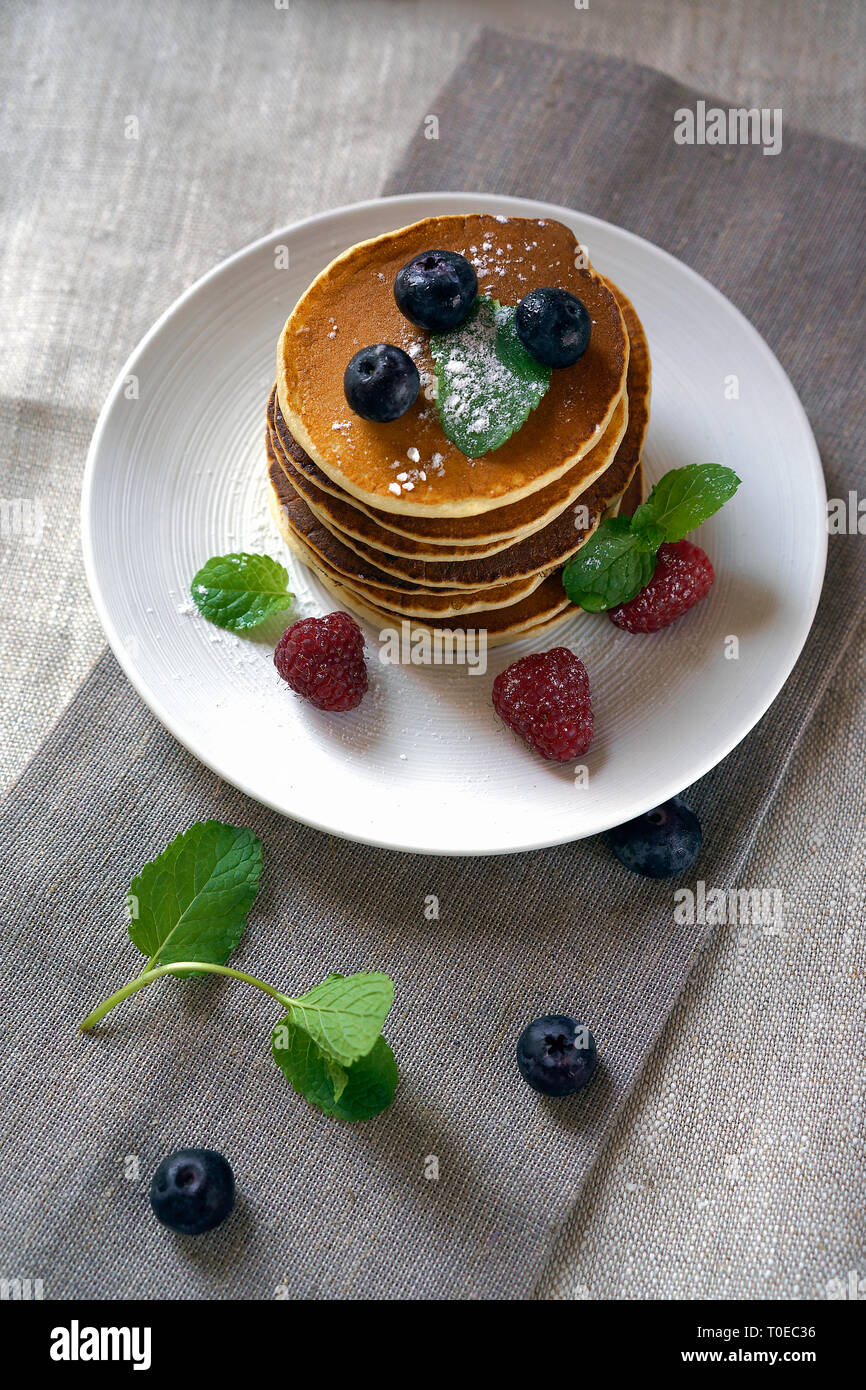 Frittelle fatte in casa con i frutti di bosco i frutti di bosco sul tavolo bianco. I pancake freschi sulla piastra tovaglia. I mirtilli, lamponi, menta sulle frittelle. Foto Stock