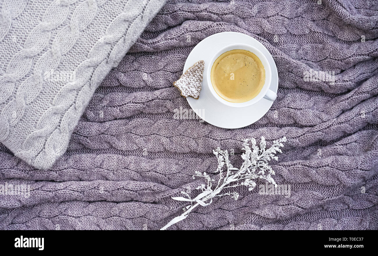White tazza di caffè con i cookie nella forma di abete e bel fiore bianco sul cuscino e calda lana rosa grigio plaid. Tessile lavorato a maglia con motivo a treccia. Autunno Inverno concetto di comfort e relax. Foto Stock