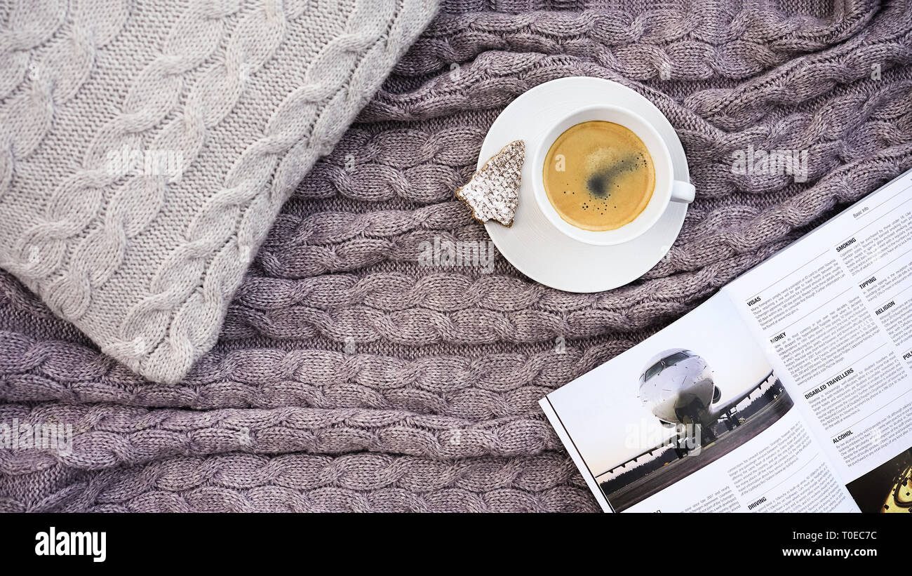 White tazza di caffè con i cookie nella forma di abete e telefono bianco fiore sul cuscino grigio e calda lana rosa grigio plaid. Tessile lavorato a maglia con motivo a treccia. Autunno Inverno concetto di comfort Foto Stock