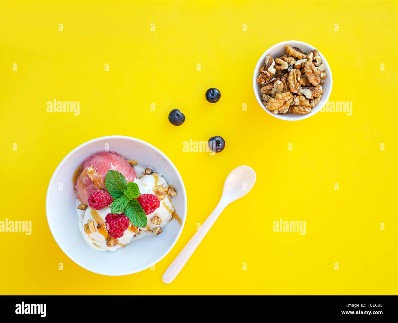 Vanila e gelato alla fragola con caramello e menta su bianco ciotola con dadi e mirtilli su sfondo giallo. Tre convogliatori, splendidi dessert. Scatto dall'alto. Foto Stock
