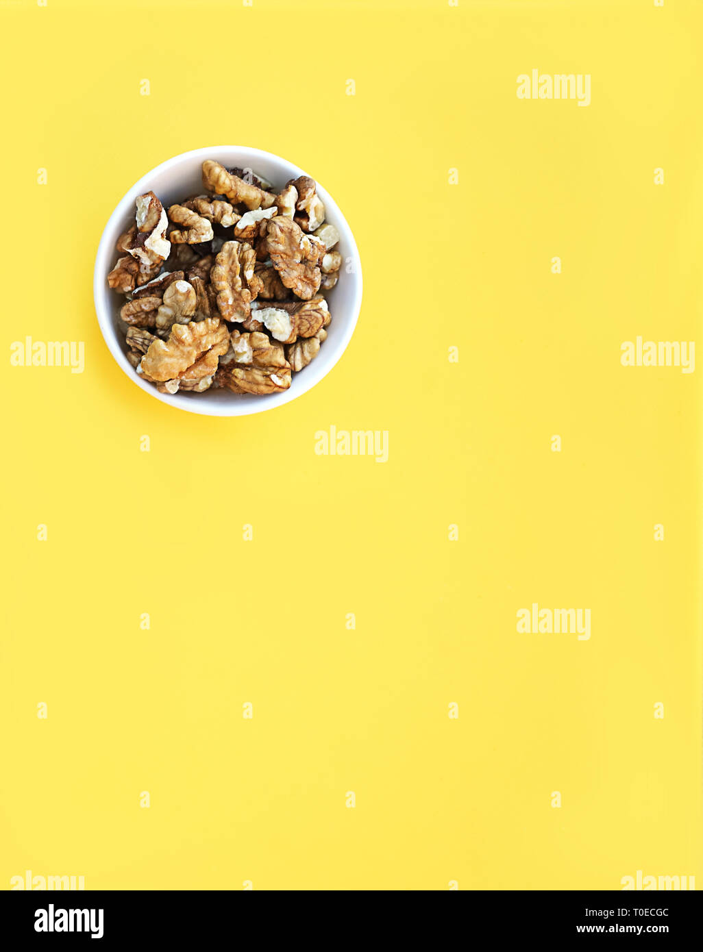 Ciotola bianca con i dadi su sfondo giallo. Scatto dall'alto. Foto Stock