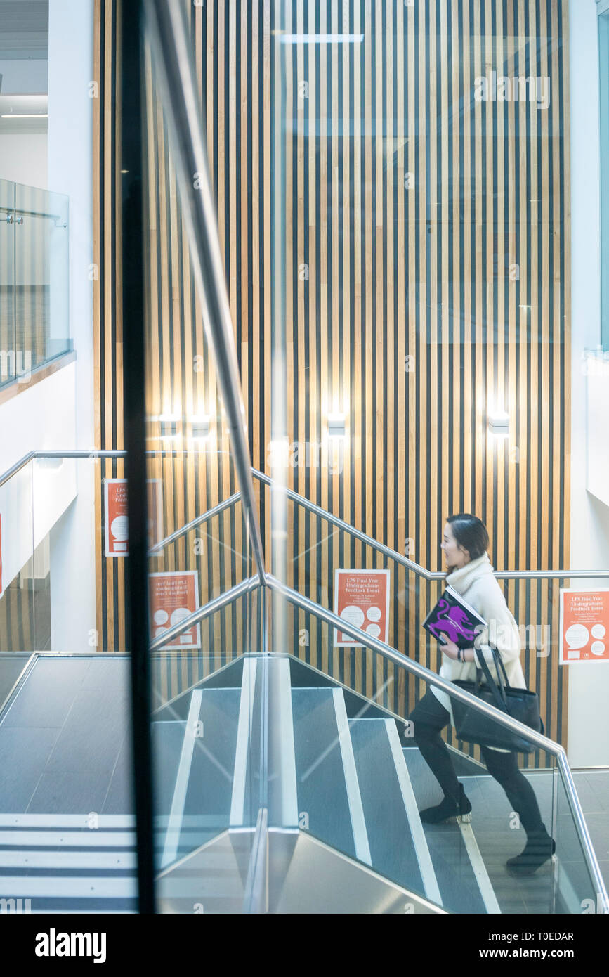 Una femmina di studenti asiatici passeggiate attraverso le diverse aree comuni all'interno di un edificio universitario Foto Stock