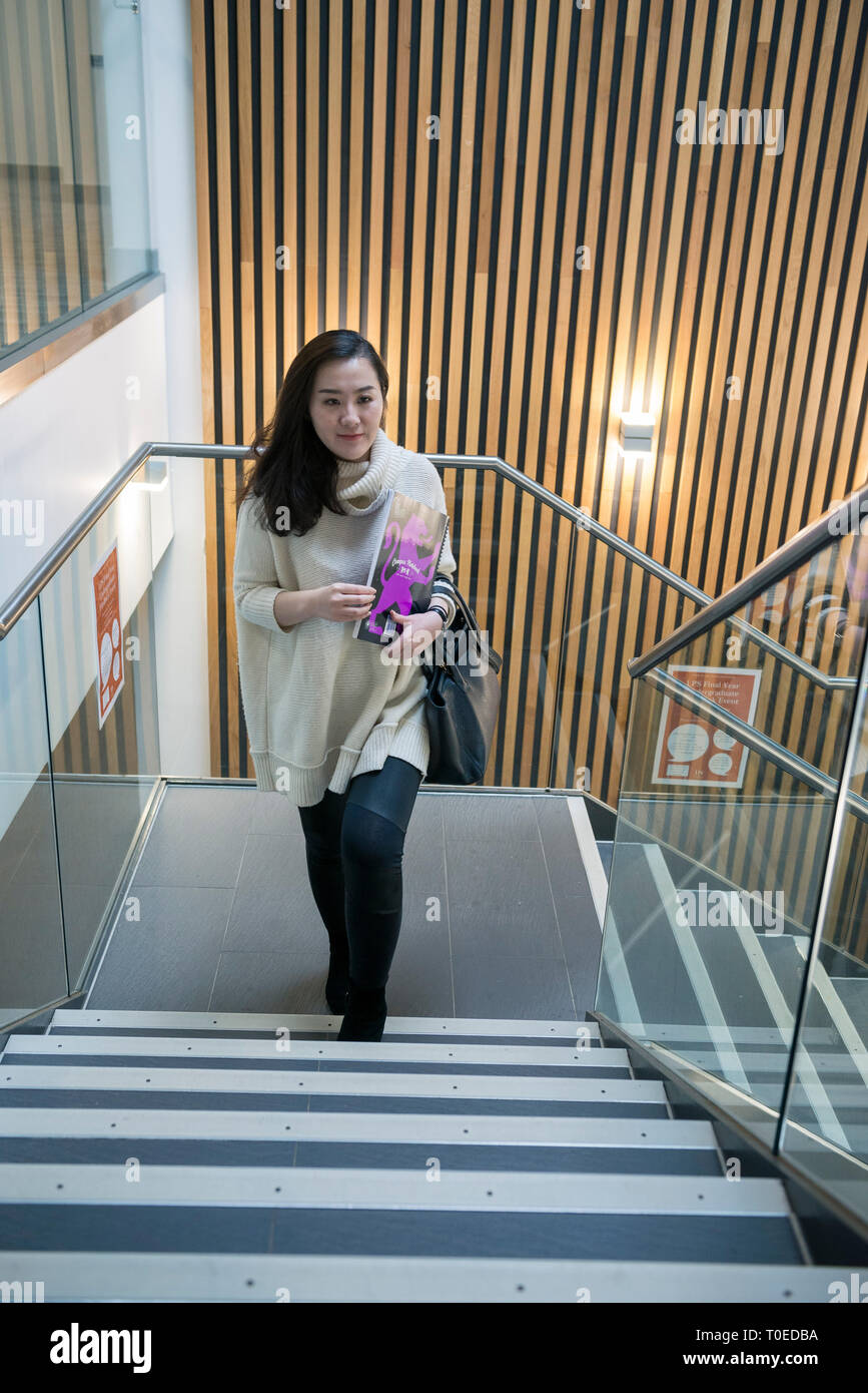 Una femmina di studenti asiatici passeggiate attraverso le diverse aree comuni all'interno di un edificio universitario Foto Stock