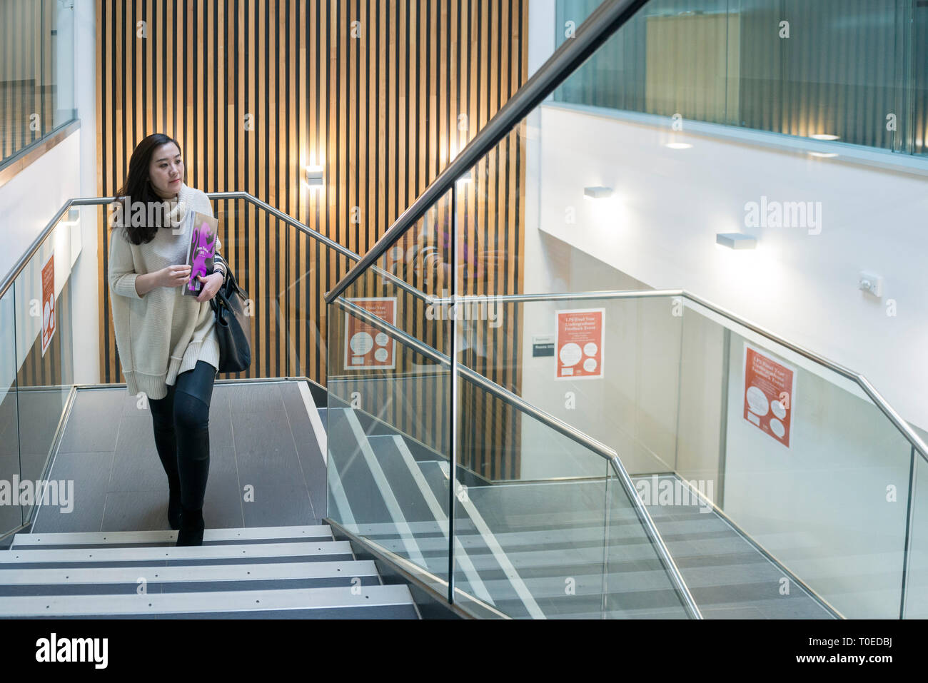 Una femmina di studenti asiatici passeggiate attraverso le diverse aree comuni all'interno di un edificio universitario Foto Stock