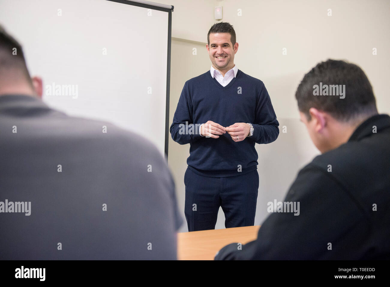 Un uomo bianco in un ponticello blu contiene una presentazione del corso di formazione per i compagni lavoratori in un ufficio sala riunioni Foto Stock