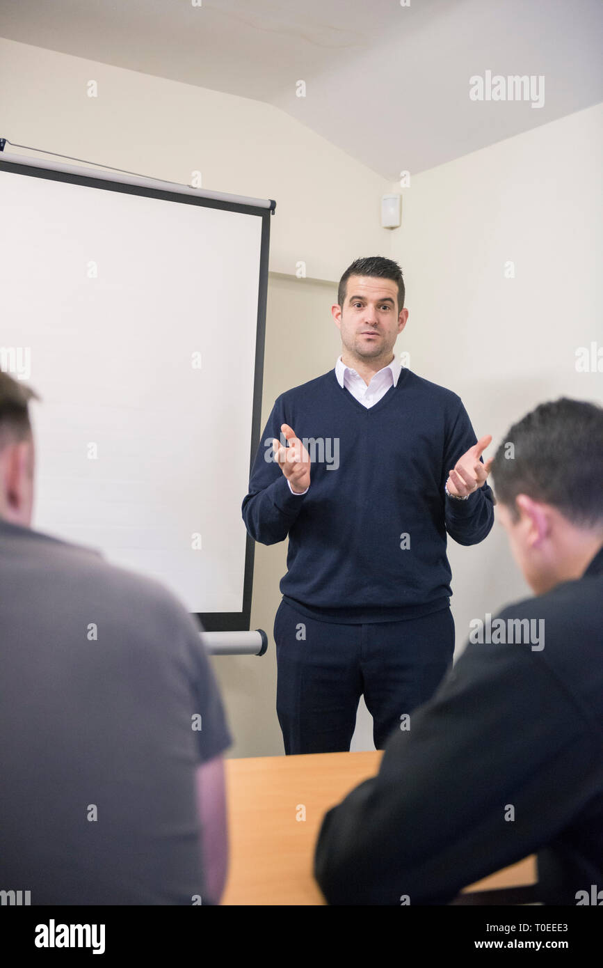Un uomo bianco in un ponticello blu contiene una presentazione del corso di formazione per i compagni lavoratori in un ufficio sala riunioni Foto Stock