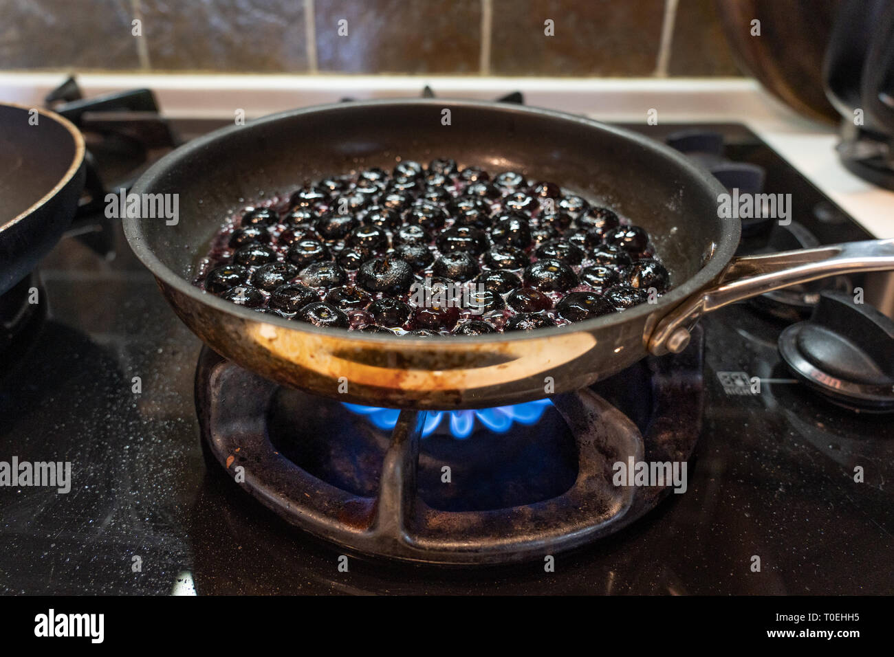 La salsa di mirtilli essendo realizzata sulla stufa in una padella in cucina per il dessert Foto Stock
