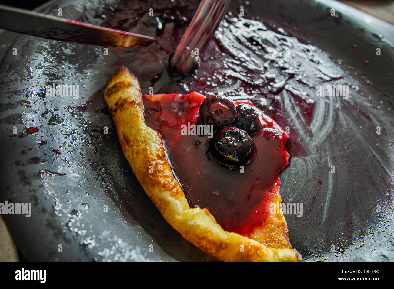 Mangiare un pancake con salsa di mirtilli Foto Stock