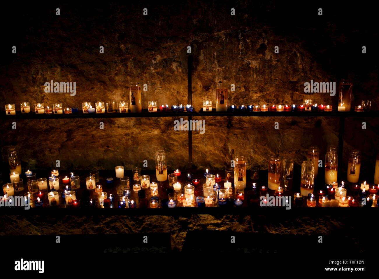 Un bellissimo display di centinaia di candele votive di varie dimensioni illuminazione di un oscuro angolo della chiesa in Francia Foto Stock