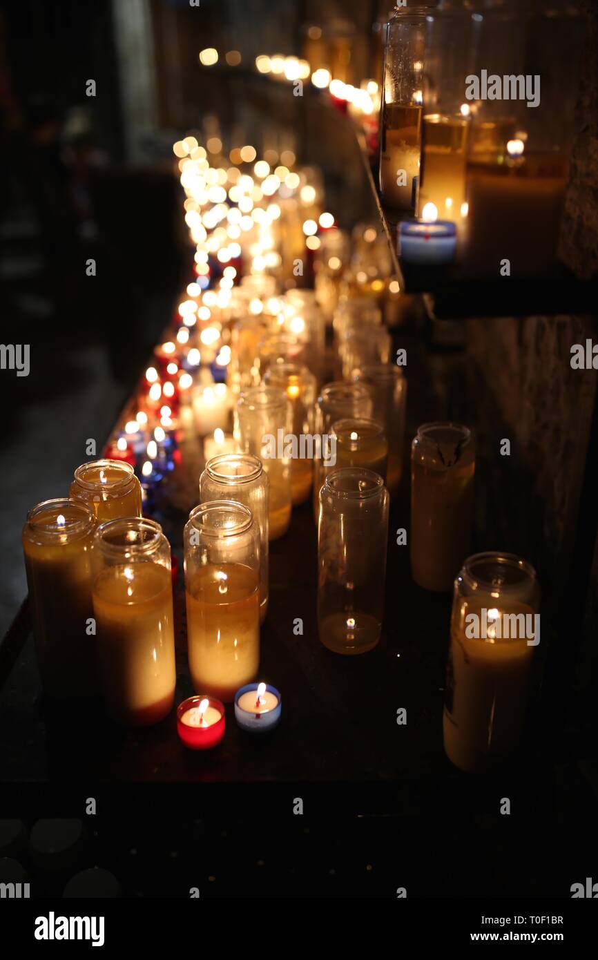 Una bella fila di bianco di sfarfallio candele votive illuminano una chiesa oscura Foto Stock