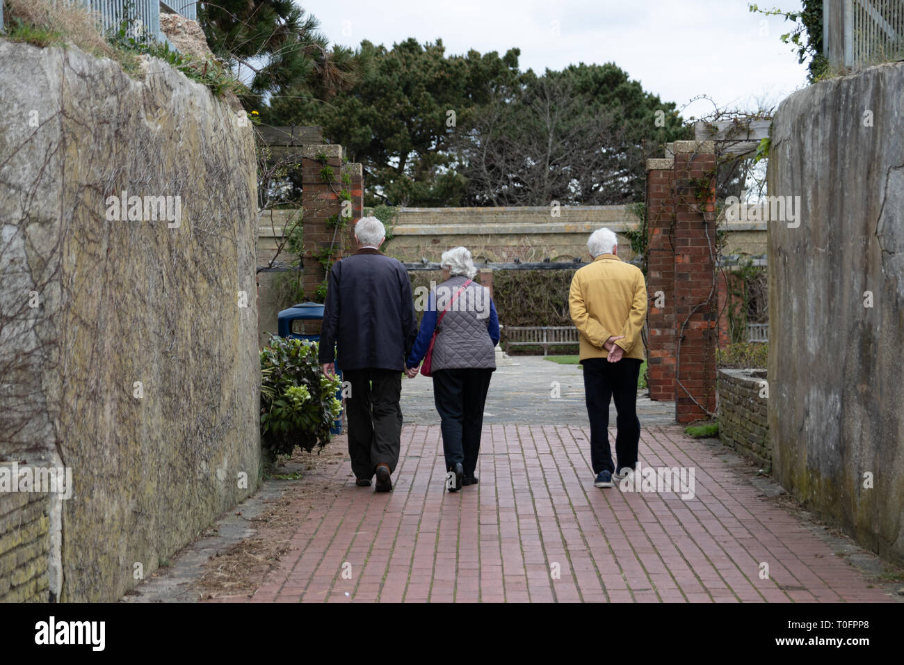 Le persone anziane a piedi in entrata di un giardino pubblico, di cui due sono tenendo le mani Foto Stock