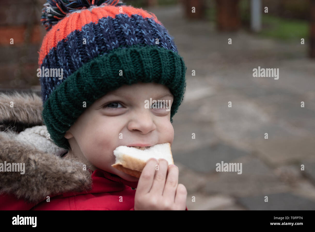 Piccolo Ragazzo di mangiare un panino indossando cappotto invernale e bobble hat Foto Stock