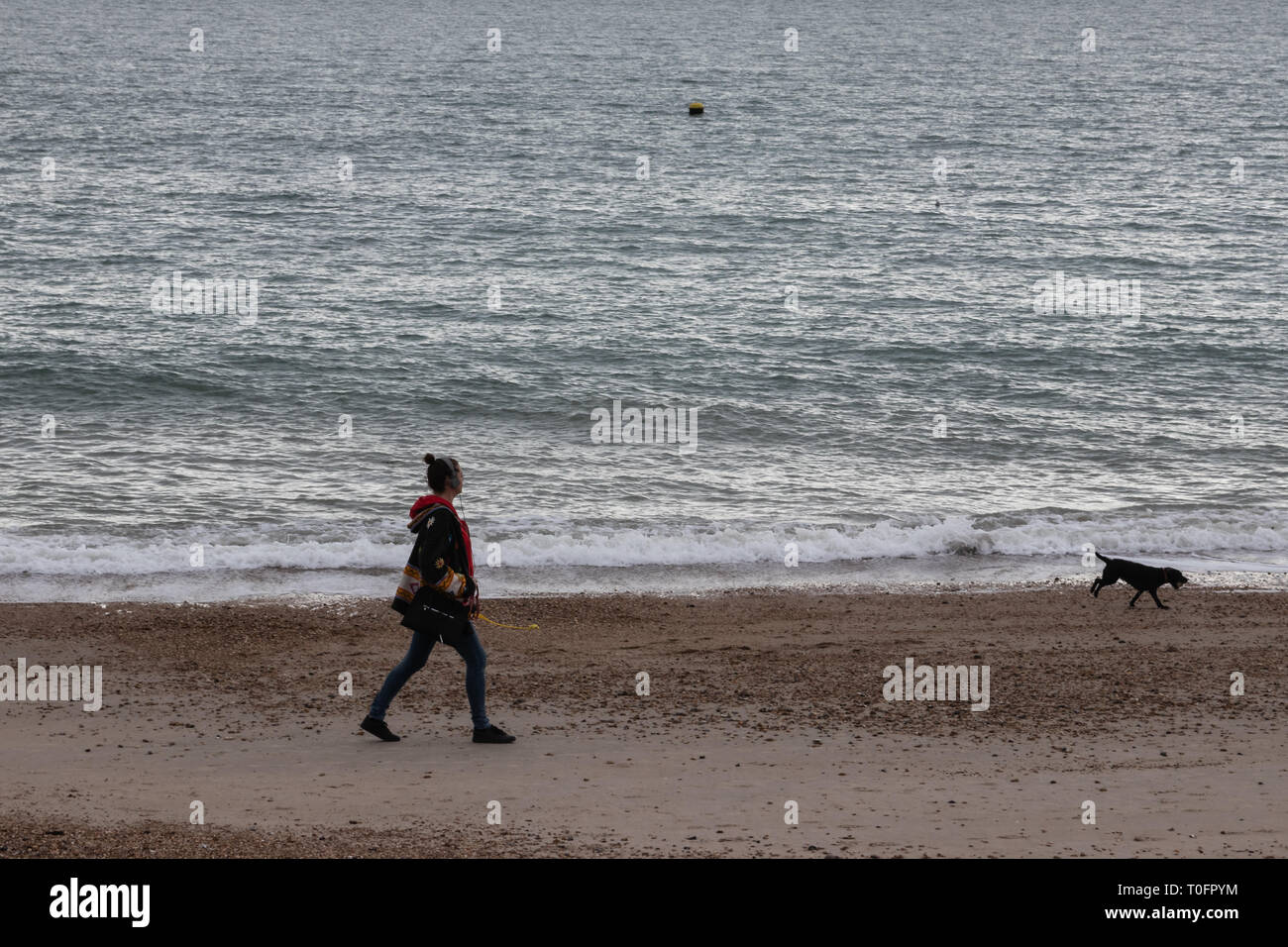 Giovane donna nel suo 30's a piedi il suo cane su una spiaggia britannico Foto Stock