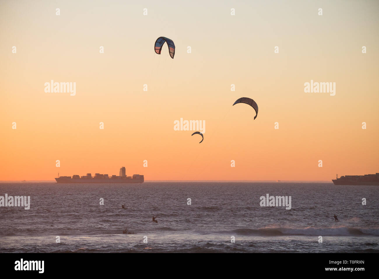 Kitesurfisti o sagome kiteboarders al tramonto sul mare con due navi cisterna o navi in background a Bloubergstrand, Cape Town, Sud Africa Foto Stock