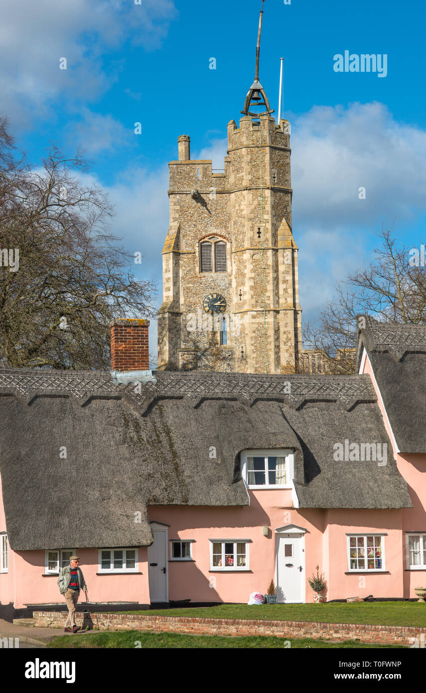 Cottage con il tetto di paglia dipinta in Suffolk rosa con Santa Maria Vergine la Chiesa sul verde villaggio. Cavendish, Suffolk, East Anglia, UK. Foto Stock