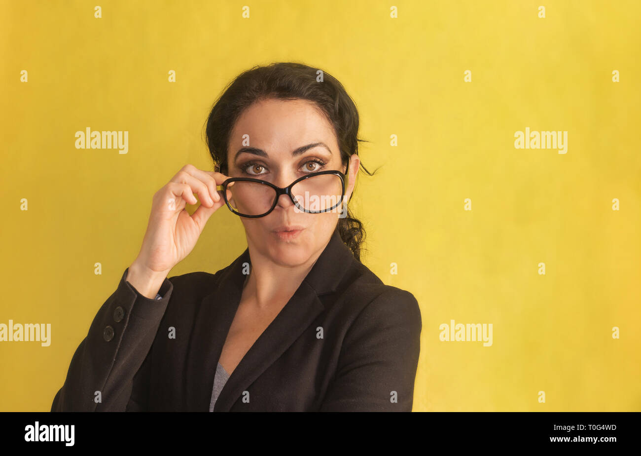 Wow. Giovane e bella donna d'affari, con spiralina, occhiali e giacca nera, isolata su uno sfondo. Sorpreso, stordito. Positivo emozione umana Foto Stock