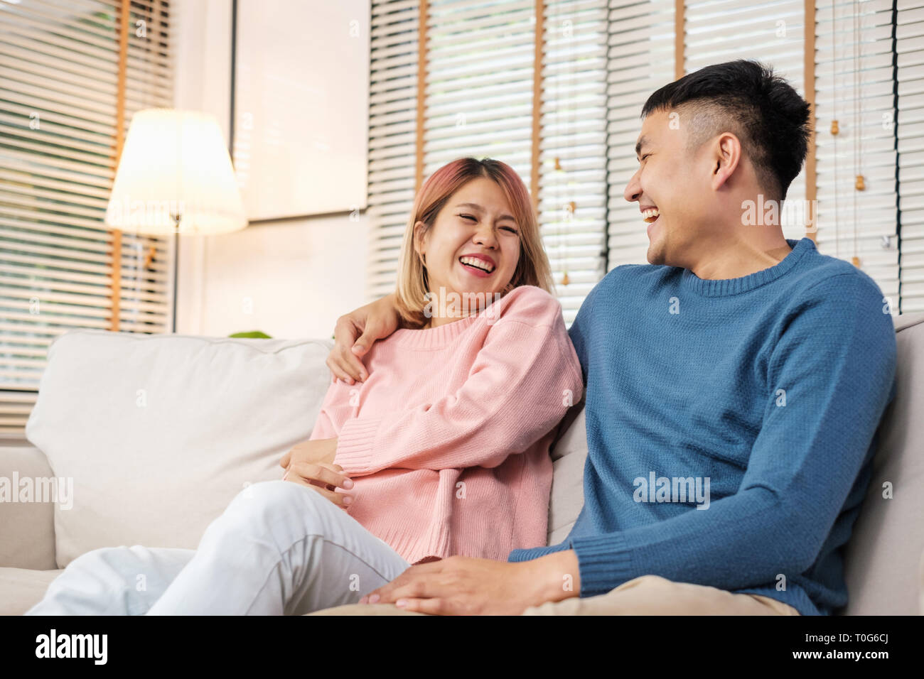 Asian giovane abbracciando e ridere mentre è seduto al divano in casa.amante matura nel concetto di casa Foto Stock