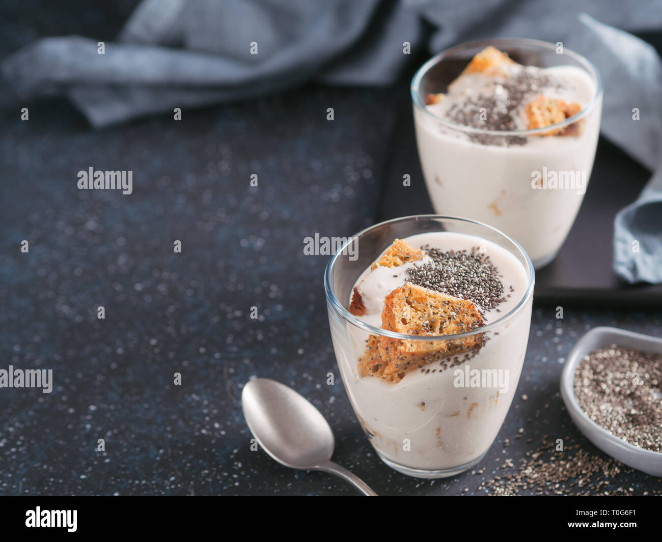 Nessuna cotta dessert cheesecake con carote tritati biscotti e chia semi in un barattolo di vetro su uno sfondo scuro. Idee e ricette per una sana prima colazione. Copia spazio per il testo. Foto Stock