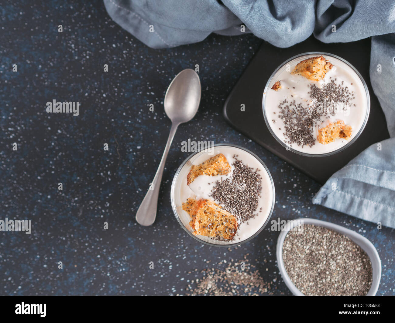 Nessuna cotta dessert cheesecake con carote tritati biscotti e chia semi in un barattolo di vetro su uno sfondo scuro. Idee e ricette per una sana prima colazione. Copia spazio per il testo. Vista superiore o flat-lay. Foto Stock
