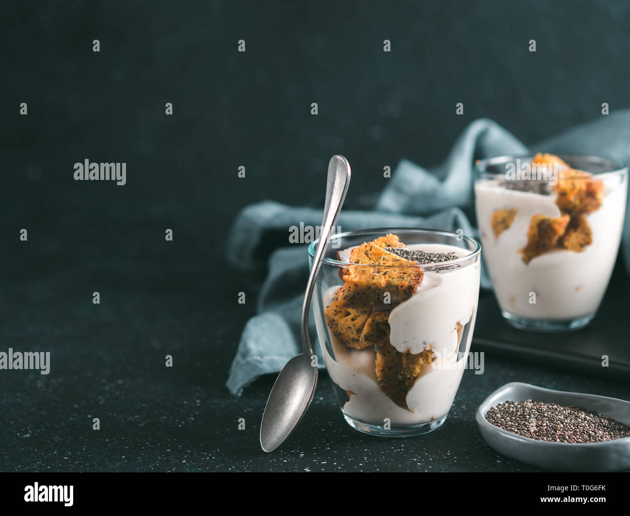 Nessuna cotta dessert cheesecake con carote tritati biscotti e chia semi in un barattolo di vetro su uno sfondo scuro. Idee e ricette per una sana prima colazione. Copia spazio per il testo. Foto Stock