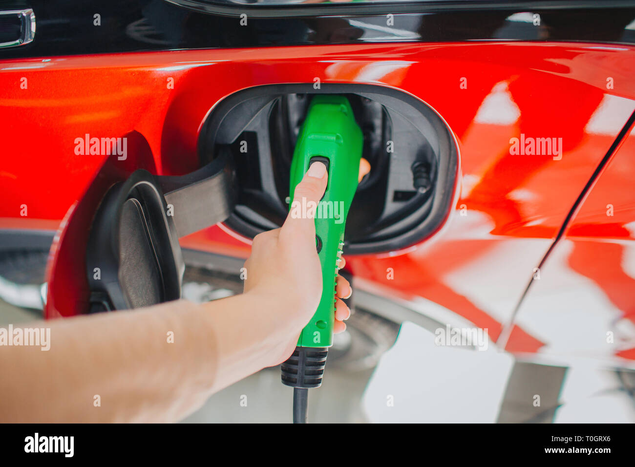 Il veicolo elettrico stazione di carica. Close-up di donna mano carica di un auto elettrica con la potenza di alimentazione del cavo collegato alla presa di corrente. Eco-friendly auto concept Foto Stock