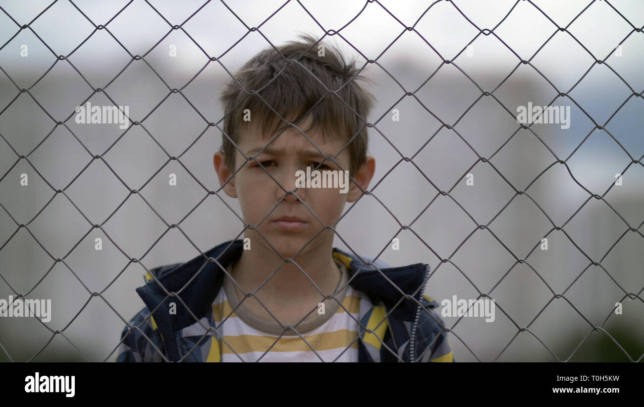 Angry boy dietro una recinzione in ferro guarda con odio verso la telecamera, bad boy Foto Stock