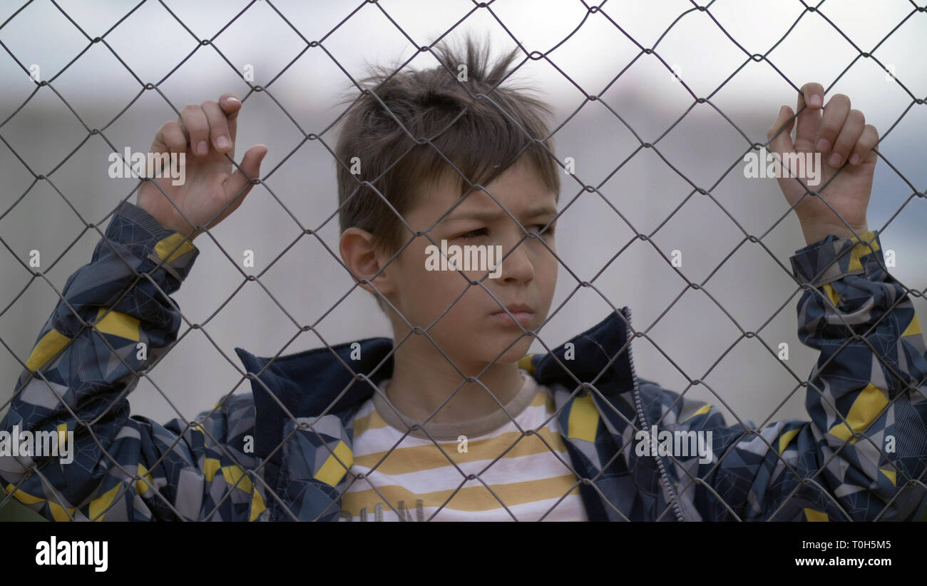 Angry boy dietro una recinzione in ferro guarda con odio, bad boy Foto Stock