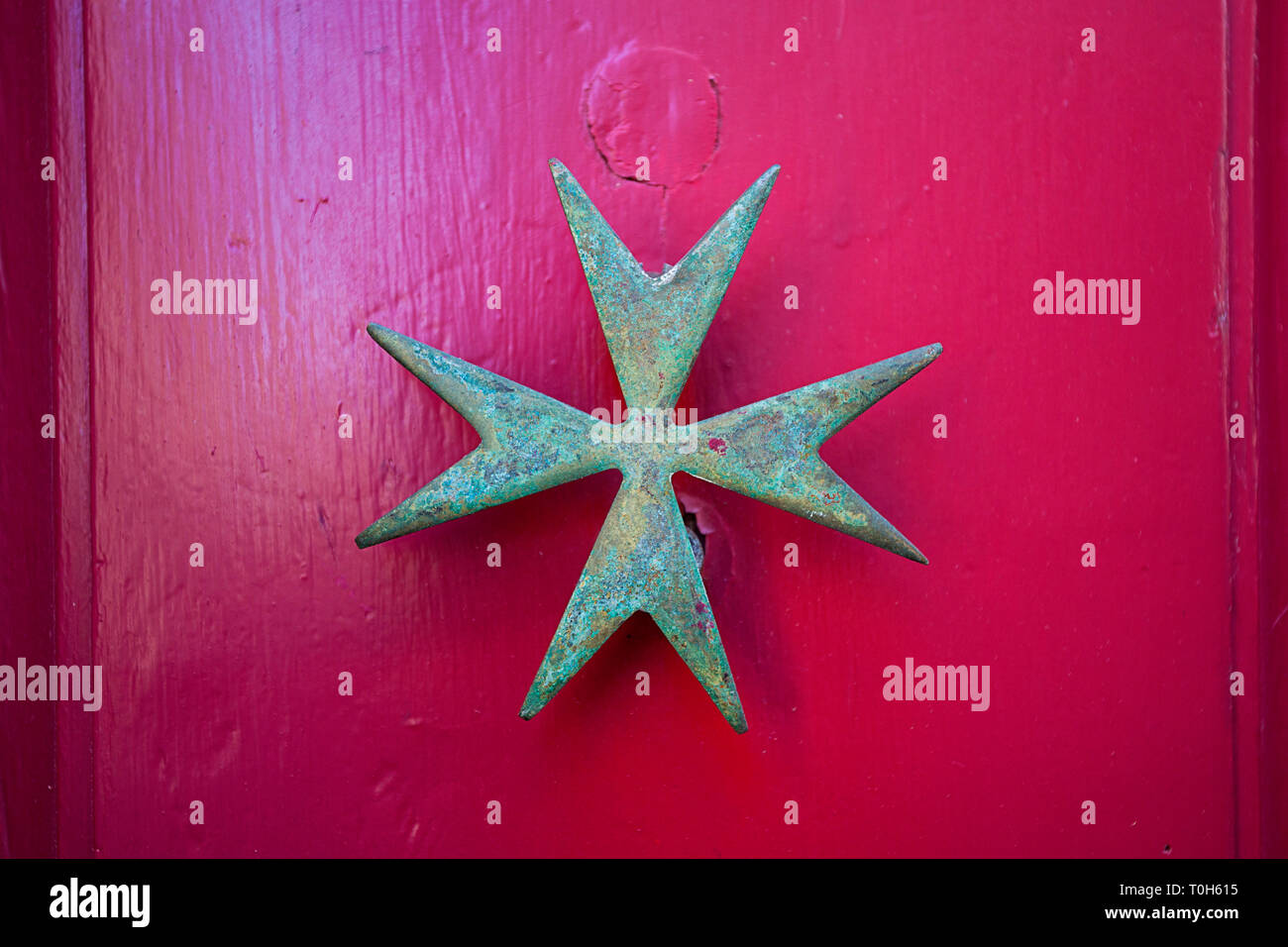 Metallo Croce Maltese su una porta rosa Foto Stock