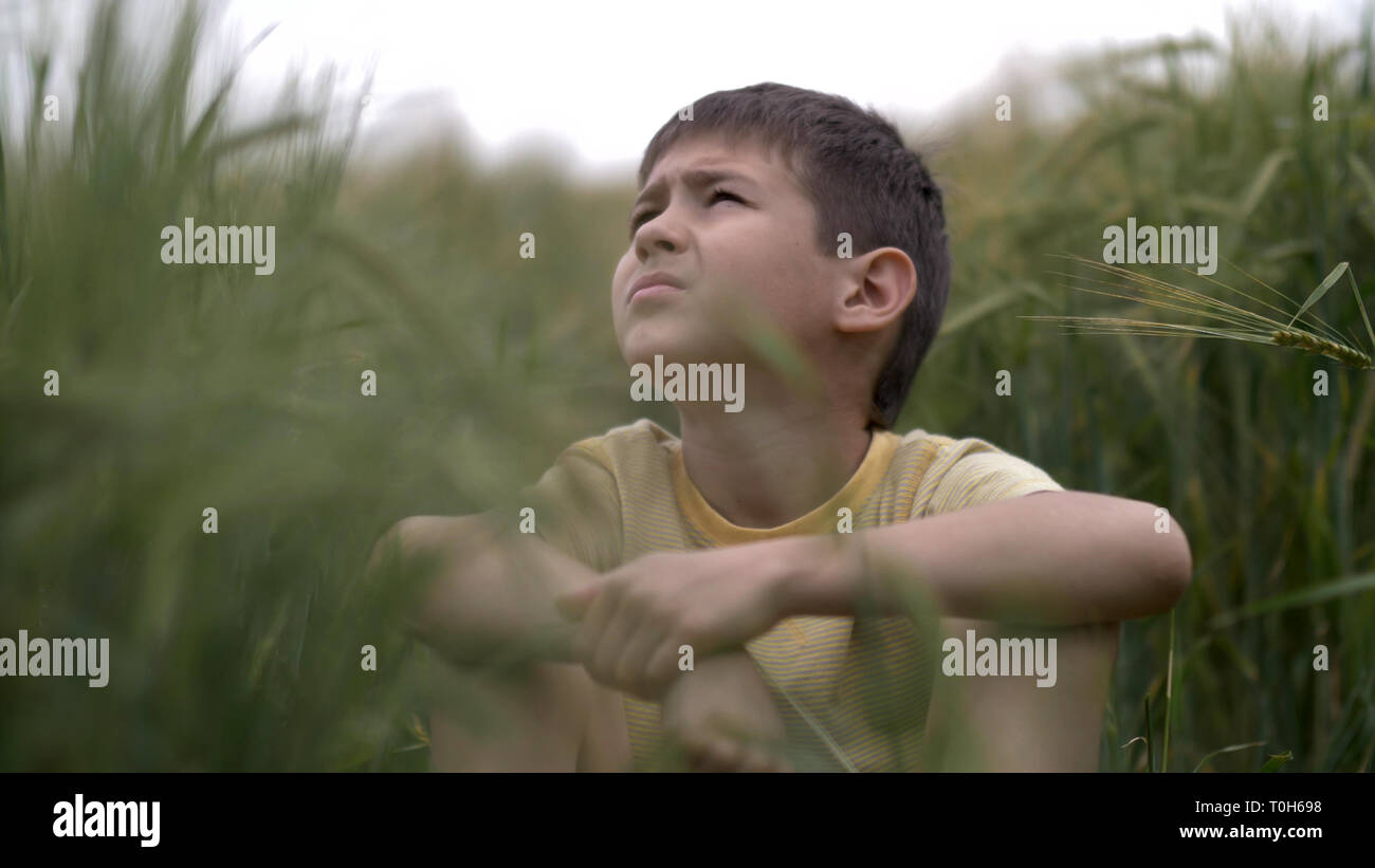 Ragazzo serio con un tence sintesi è seduta nel campo guardando il cielo Foto Stock