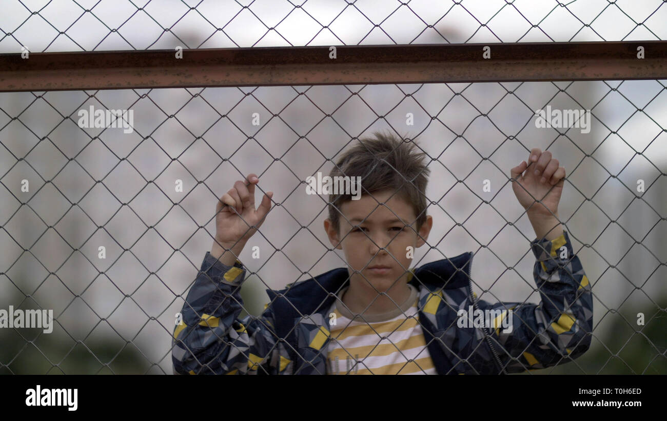 Offeso boy dietro una recinzione in ferro guardare la fotocamera Foto Stock