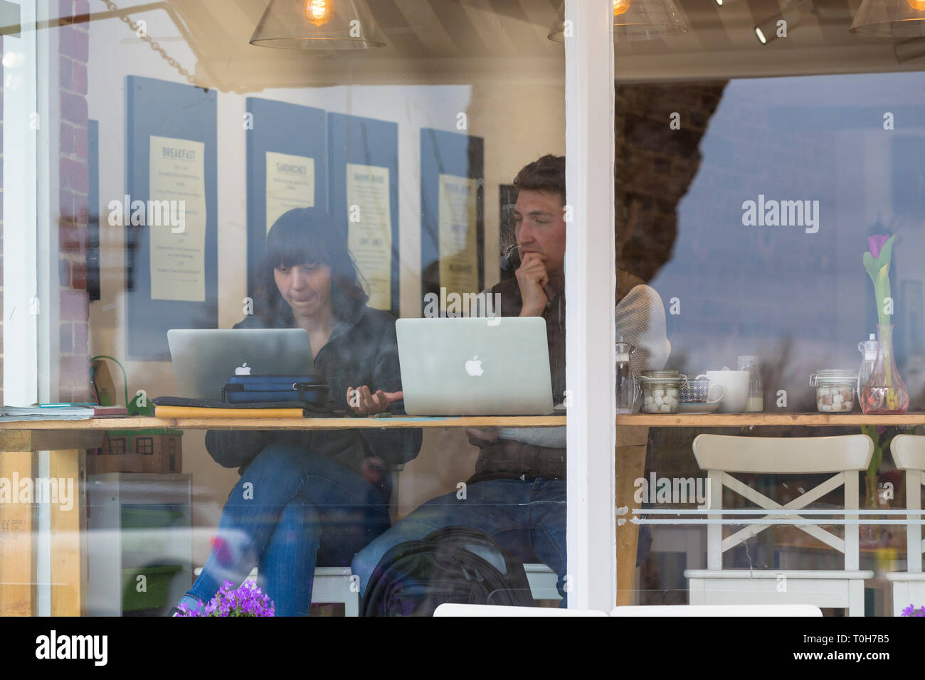Coppia giovane con Apple Mac in un negozio di caffè seduti a una finestra bar, Regno Unito Foto Stock